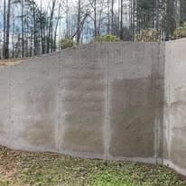 Concrete wall with a smooth finish, set against a backdrop of trees and blue sky.