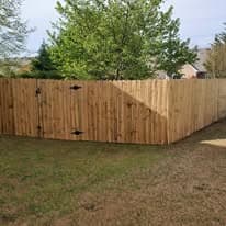 Wooden fence surrounding a yard with green trees under a clear blue sky.