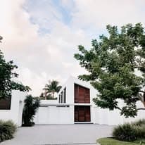 Modern white house with wooden accents and lush greenery under a cloudy sky.