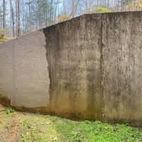 Concrete wall with uneven surface and green grass in a forested area.