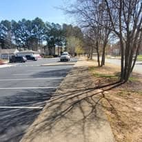Empty parking lot with trees casting shadows on a sunny day. Pathway along the side.