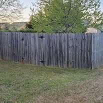 Wooden fence enclosing a backyard with green trees and grass under a clear sky.