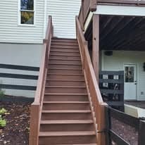 Wooden staircase leading to a deck, surrounded by landscaping and a modern home exterior.