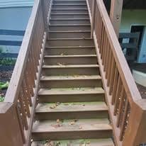 Wooden staircase with leaves scattered on steps, leading to a covered porch area.